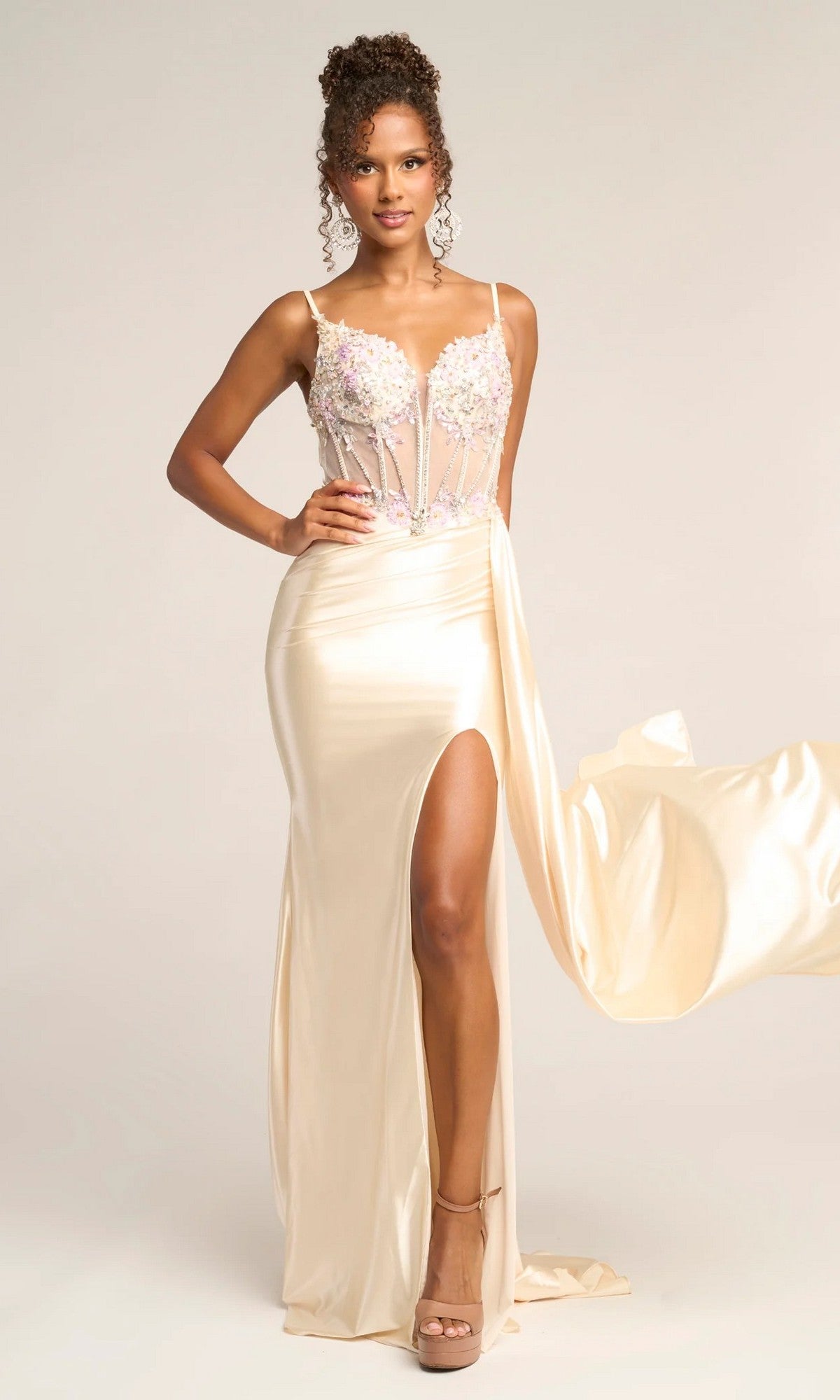 A woman models the Portia and Scarlett PS26270 long prom dress in cream, featuring a satin finish, sheer corset bodice with floral embroidery, spaghetti straps, and a high leg slit against a plain background.